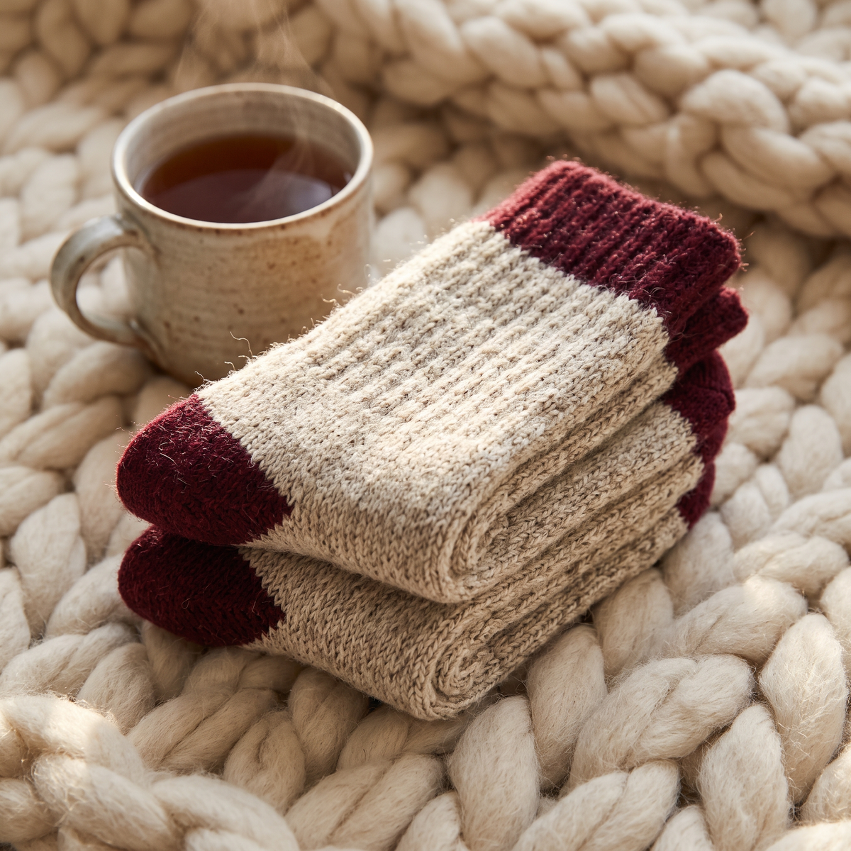 Chaussettes en laine mérinos écrues et bordeaux près d'une tasse de thé
